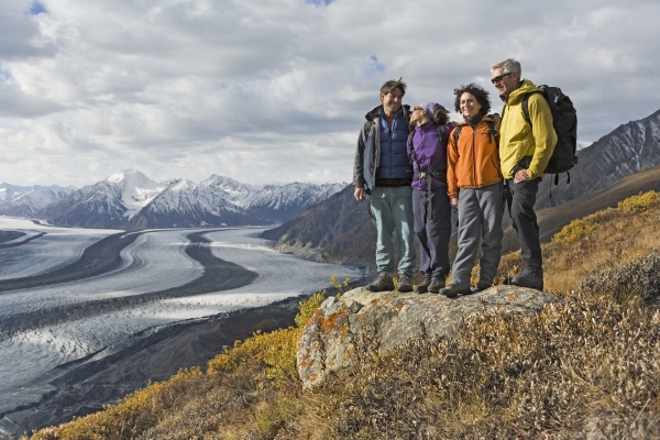 Four people in colourful winter jackets pose arm in arm at the top of a mountain vista